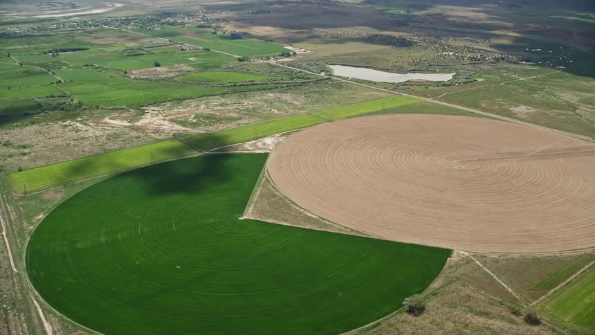 Aerial footage of Pac-man and circular crop fields passing by in Elberta Utah showcasing the beauty of rural farming in the Southwest United States during summertime