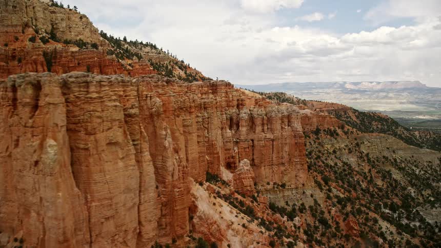 Aerial footage of Bryce Canyon National Park in Utah showcasing groups of hoodoos and mesa cliffside on a cloudy day
