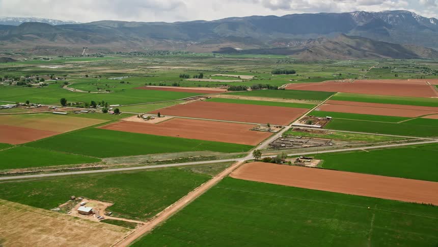 Aerial view of a rural area in Richfield Utah with farmland mountains and country roads amidst partly cloudy skies during summer