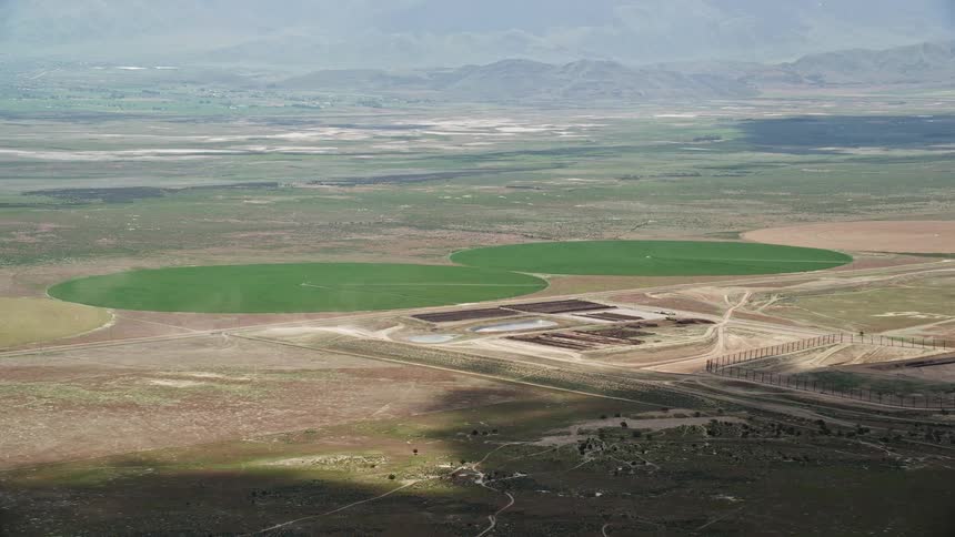 Aerial footage showcasing two green circular crop fields in Elberta Utah with a rustic and agricultural landscape during the summer daytime