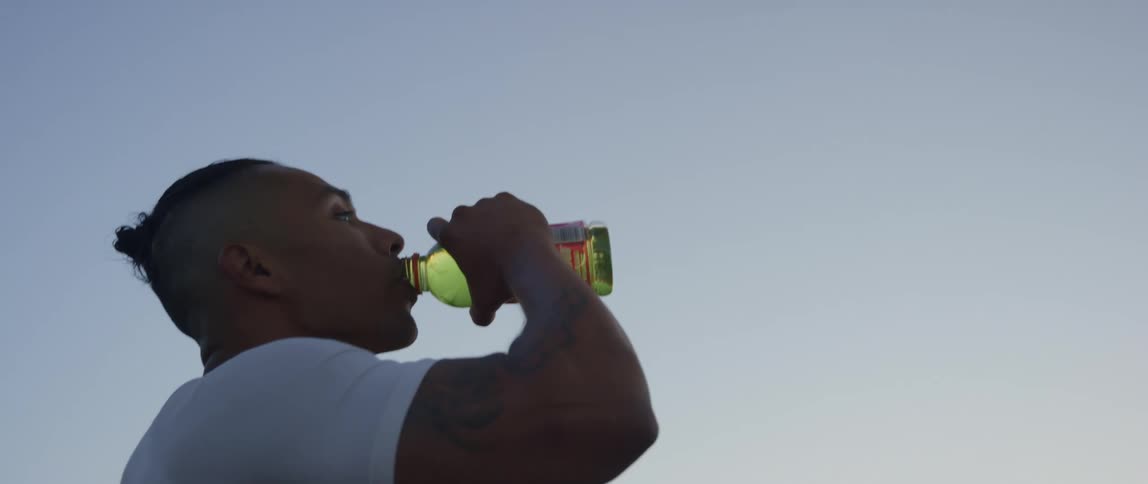 Close up of a man drinking out of a bottle outdoors at dusk