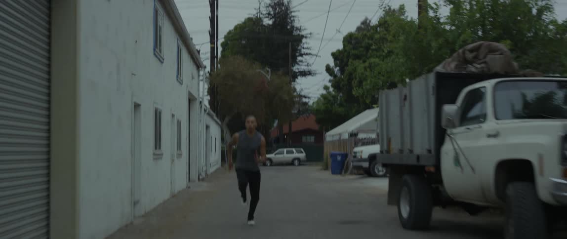 A black man running on a path past houses and cars