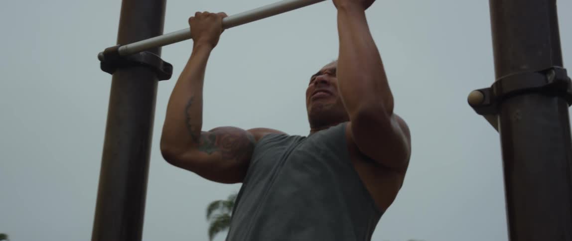A black man doing pullup in a yard at midday