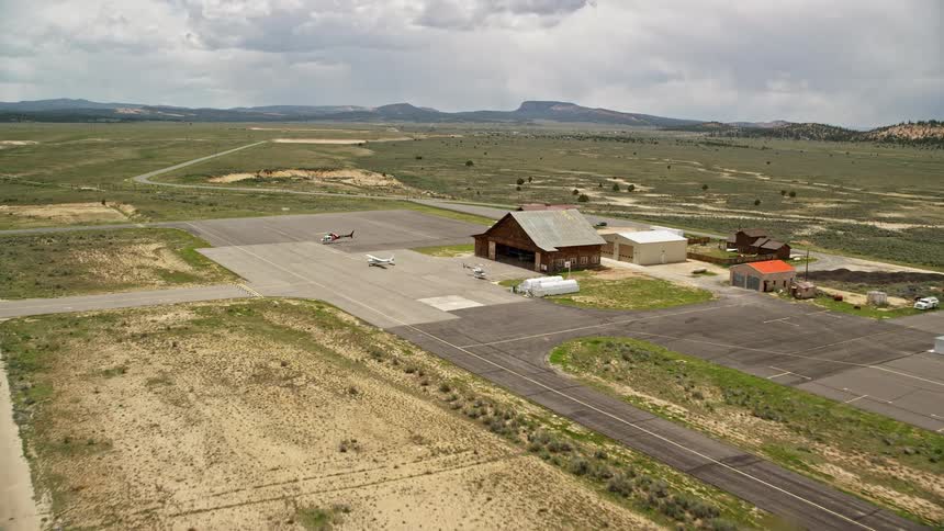 Approaching a single prop plane helicopters and a wooden hangar at Bryce Canyon Airport in Utah during a partly cloudy summer day