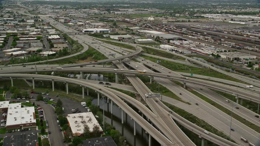 Aerial view of approaching and flying over I-80 and I-15 interchange in Salt Lake City Utah during summer with light traffic and partly cloudy skies