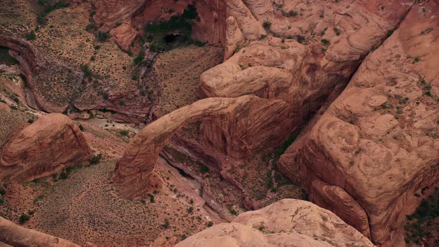  aerial footage of Rainbow Bridge National Monument a natural stone bridge surrounded by arid landscapes and rock formations with a view of the riverbed and the Southwest canyons captured during a partly cloudy day in the summertime