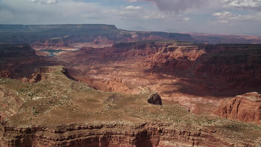 Wide aerial view of a dry riverbed in a canyon on the Navajo Nation Reservation Utah revealing the arid landscape table mountains and partly cloudy skies during summertime