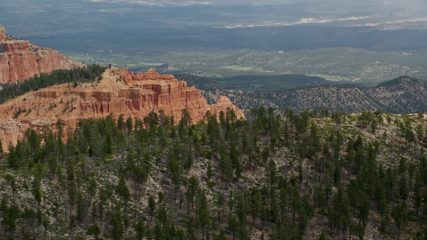 an aerial view of Bryce Canyon National Park in Utah showcasing massive canyon peaks lush vegetation and a mountain range and plains in the horizon