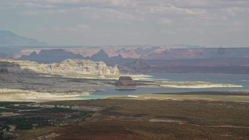 Aerial footage of Lone Rock and Lake Powell in Glen Canyon National Recreation Area showcasing the arid landscape and water body surrounded by mountains in southwest Utah and Arizona during the summer