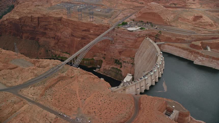 Aerial footage of Glen Canyon Dam and Bridge in Arizona capturing the breathtaking views of the Colorado River arid landscape and the power generation infrastructure on a sunny day in the Southwest region of the United States during summer