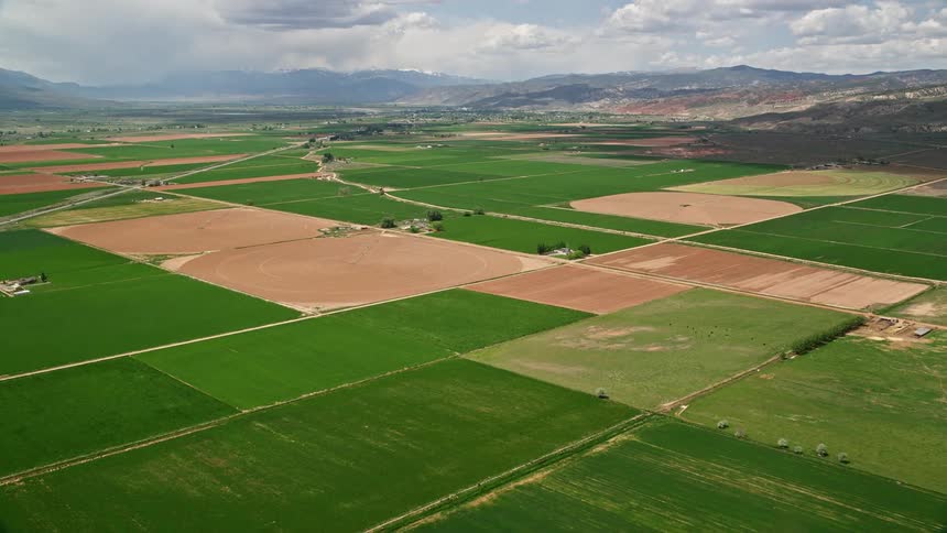 Aerial footage showcases agricultural area with crops mountain range and a country road in Richfield Utah during the summer