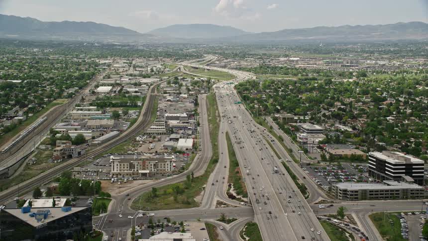 Aerial footage of cars moving on I-15 and passing homes in Salt Lake City Utah during a partly cloudy summer day