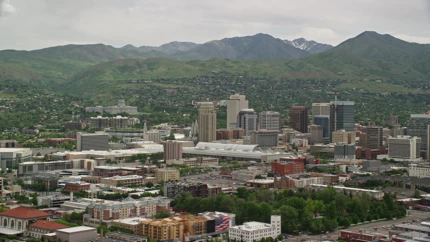 an aerial view of Downtown Salt Lake City and the Utah State Capitol showcasing the metropolis surrounded by mountain ranges on a bright and cloudy day