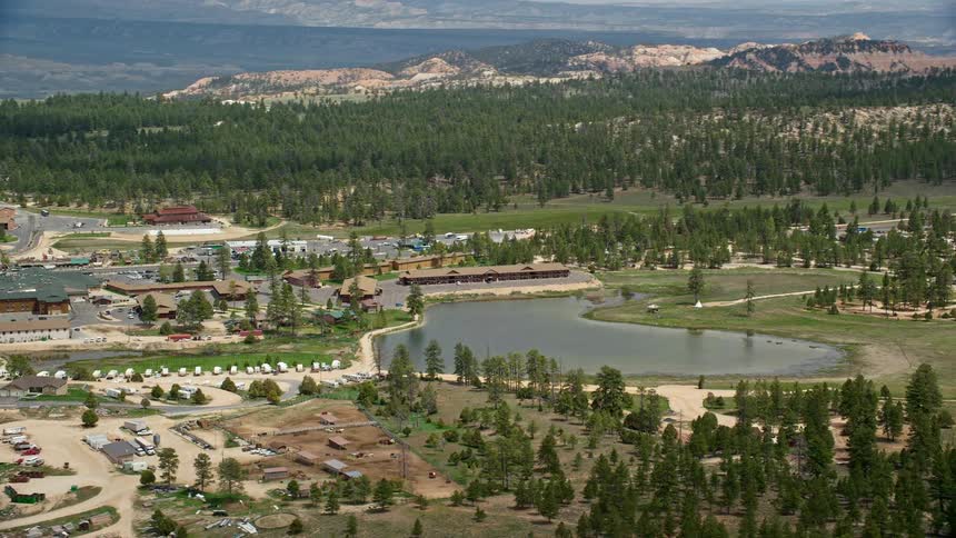 Aerial footage of a small town surrounded by hotels near Bryce Canyon National Park in Bryce Utah with lush green spaces and a lake