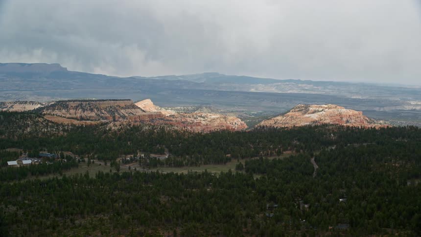 Aerial footage of Bryce Canyon National Park in Utah flying over a lush green forest with mesas in the background