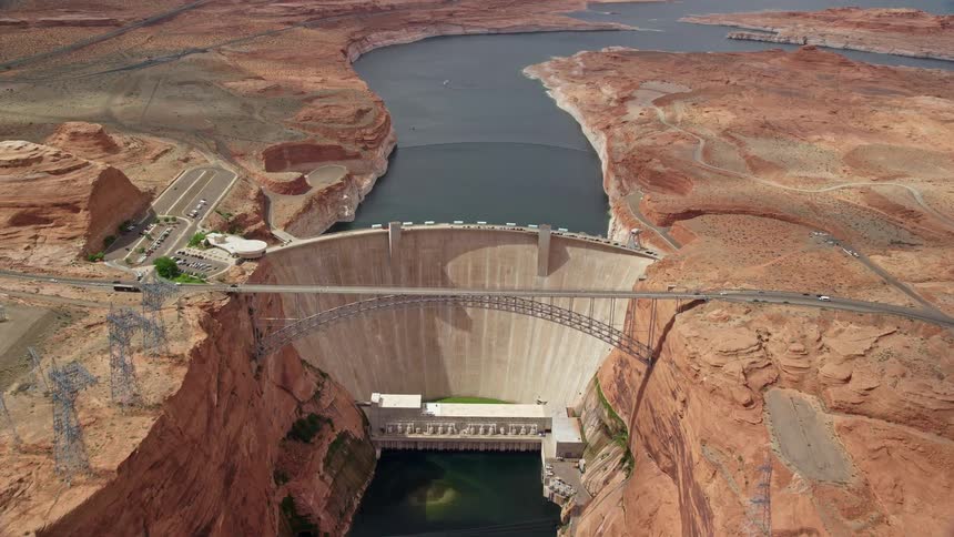  aerial footage of the Colorado River flowing towards the Glen Canyon Dam and Bridge in Arizona showcasing the grandeur of the canyon and the power generation industry | Location: Arizona Utah