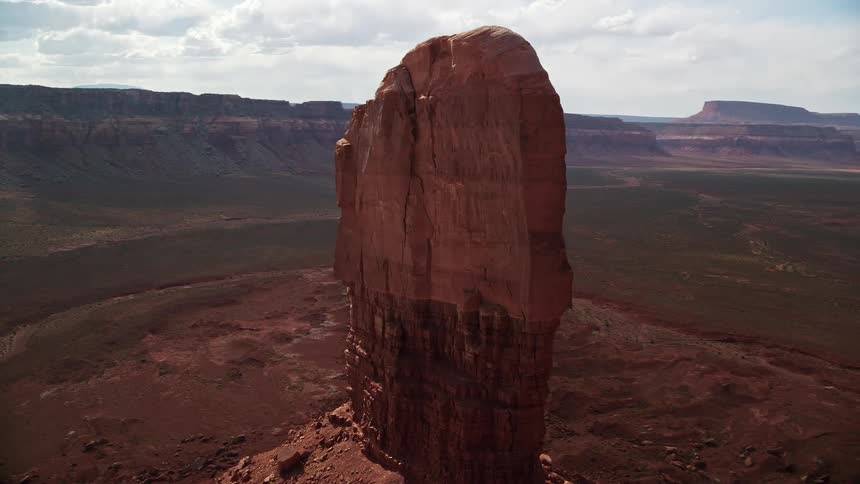 Aerial footage of a red rock formation surrounded by mesas circling the tall butte on a cloudy day in the Navajo Nation Reservation Arizona Utah