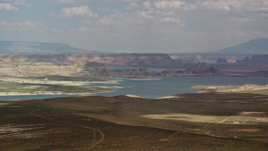 A mesmerizingaerial view of Lake Powell in Glen Canyon National Recreation Area showcasing the breathtaking landscape of flat lands mountains and a river surrounded by arid hills during a partly cloudy day in Utah and Arizona
