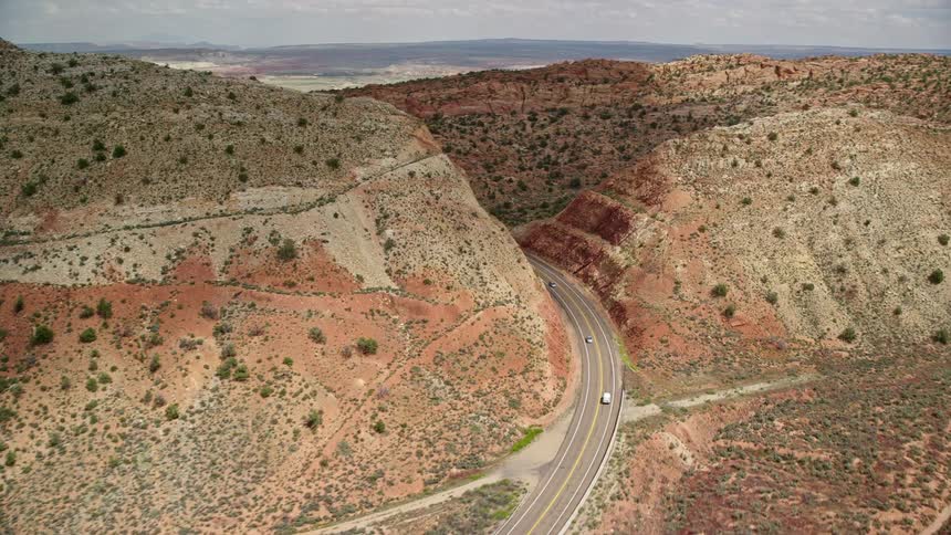 A white car is tracked on Highway 89 Glen Canyon National Recreation Area as the highway winds through a mountain canyon in the arid and partly cloudy Southwest Utah Arizona