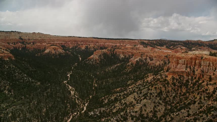  aerial footage of Bryce Canyon National Park in Utah showcasing a wide canyon with trees surrounded by hoodoos and buttes on a cloudy day highlighting the diverse vegetation