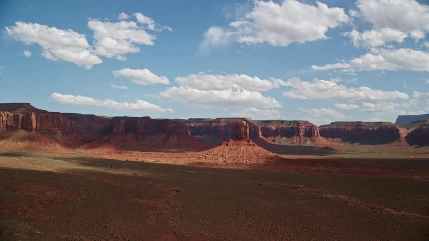 Flying towards a tall butte with mesas in the distance capturing the mesmerizing landscape of the Navajo Nation Reservation in Arizona and Utah during a partly cloudy day