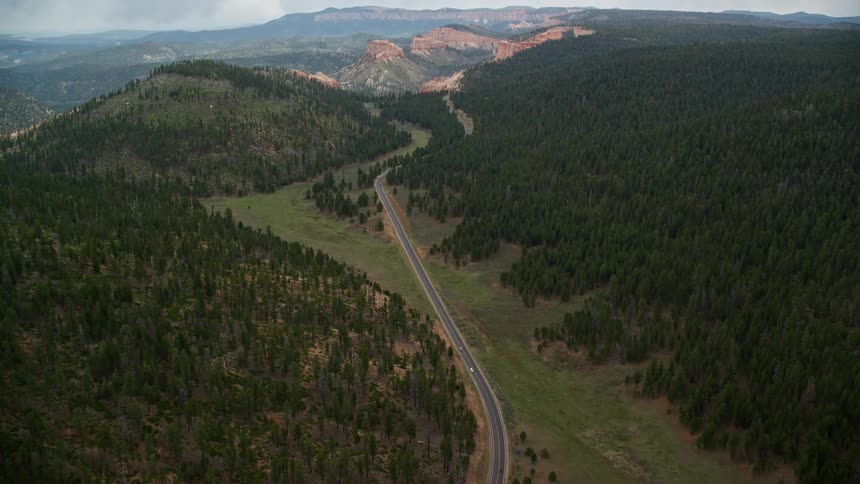 Aerial footage of a highway surrounded by pine trees in the forest approaching Bryce Canyon National Park Utah
