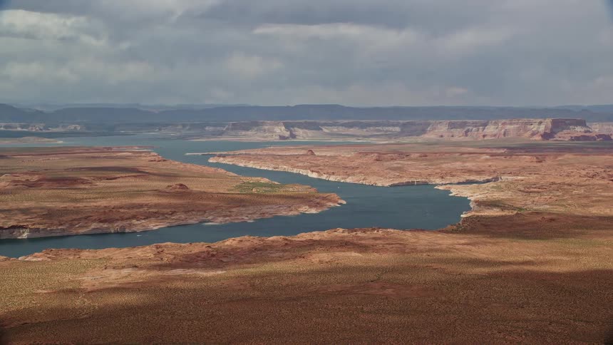  aerial footage capturing the breathtaking beauty of Lake Powell surrounded by arid desert landscapes and distant mesas in the scenic Southwest United States during a sunny summer day