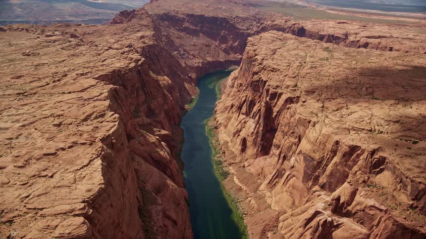 Aerial footage of the Colorado River flowing through the deep Glen Canyon in Arizona capturing the arid landscape partly cloudy skies and the natural beauty of the Southwest United States during the summer