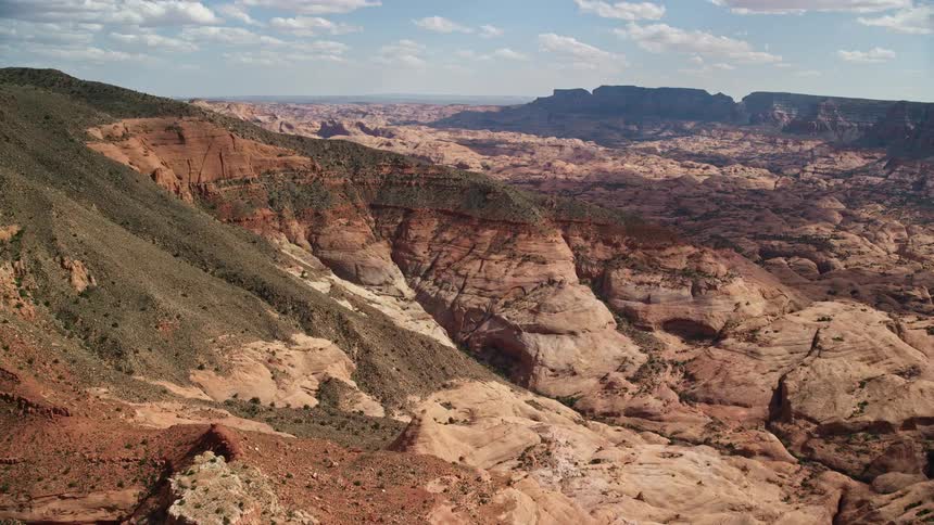 Aerial footage of flying towards Navajo Mountain peaks and slopes in Utah's Southwest capturing the natural beauty of the arid desert landscape under partly cloudy skies during a sunny day