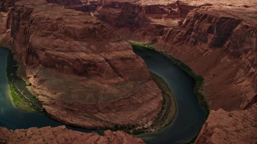  aerial footage of Horseshoe Bend and the Colorado River circling through the arid desert landscape of Glen Canyon Arizona showcasing the natural beauty of the Southwest United States during a partly cloudy summer day in Utah