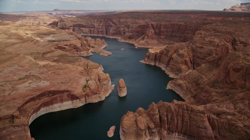  aerial footage of an approaching and flying over Lake Powell with stunning cliffs rock formations and Navajo Canyon in Arizona showcasing the arid and desert beauty of the Southwest United States during a partly cloudy summer day in Utah