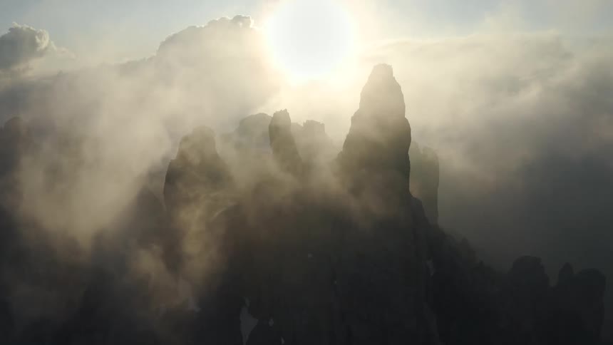 Sunlight peeks through dense clouds and fog over a canyon