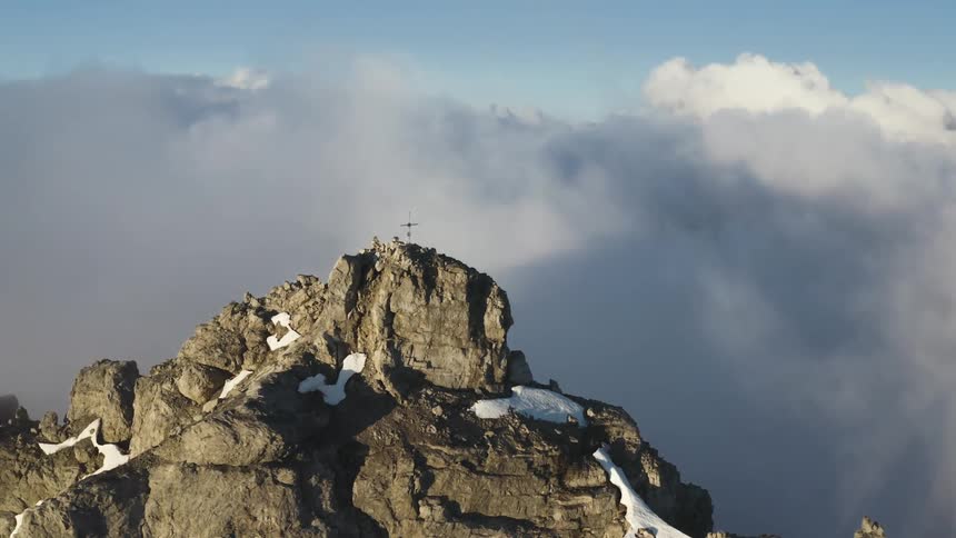 Aerial view of a cross on top of a rugged mountain over clouds
