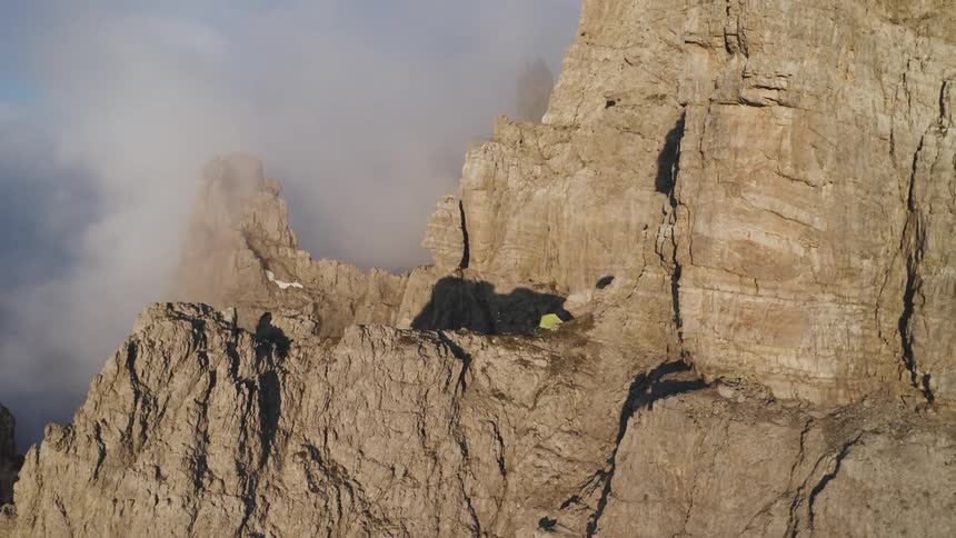 A tent erected on a small cliff high in a foggy mountain range during the day