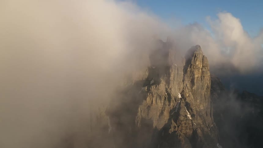 The peaks of a jagged stone mountain peaking through the fog during the day