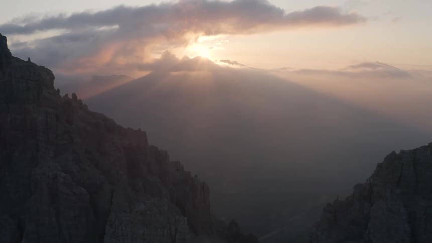 Sun shines over fog filled valley between snow speckled mountain slopes