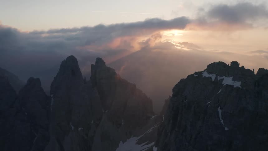 Sun shines through fog onto snow speckled mountains