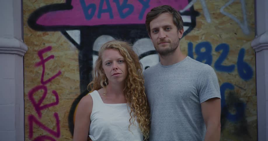 Portrait of a man and a woman looking directly into camera with graffiti behind them