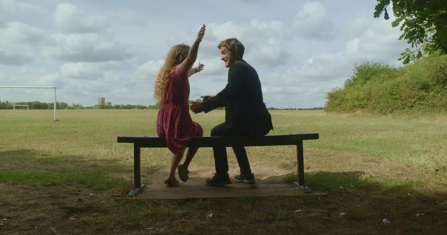A man proposes to a woman and they embrace while sitting on a bench in a park