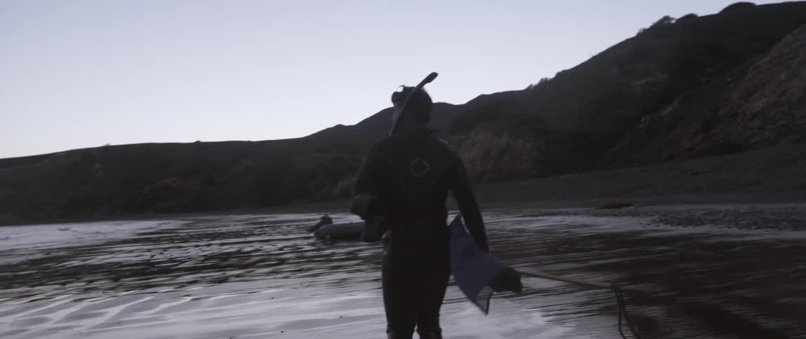 A man is walking along the beach in scuba gear