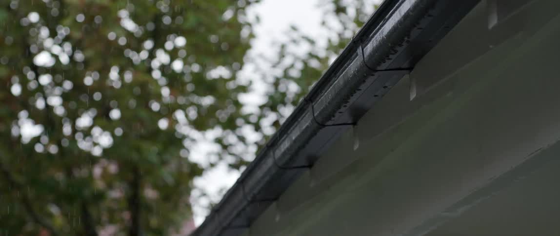 Rain falling and being drained by the gutter on the roof of a house next to a tree during day time