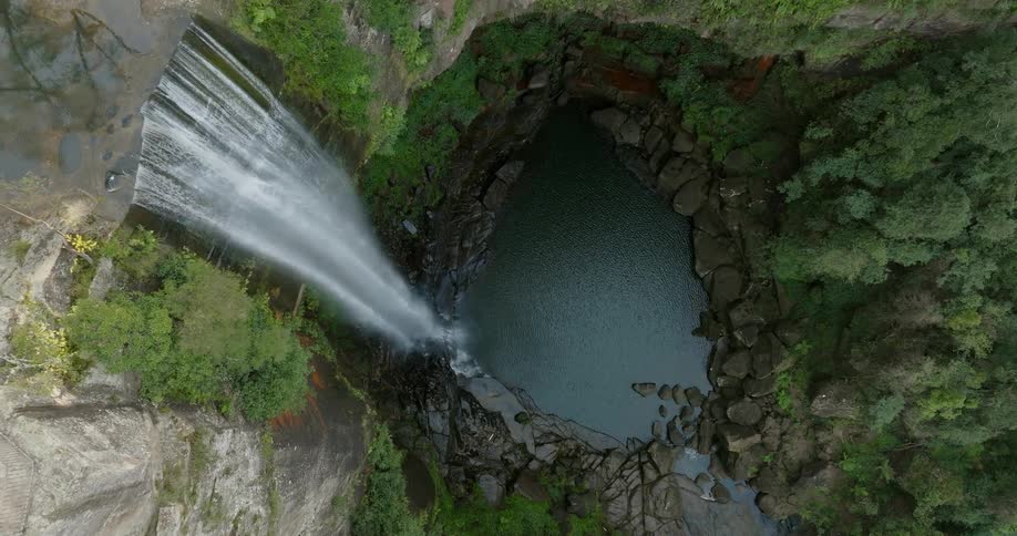 Waterfall flows down cliff into pond pool surrounded by boulders in woods