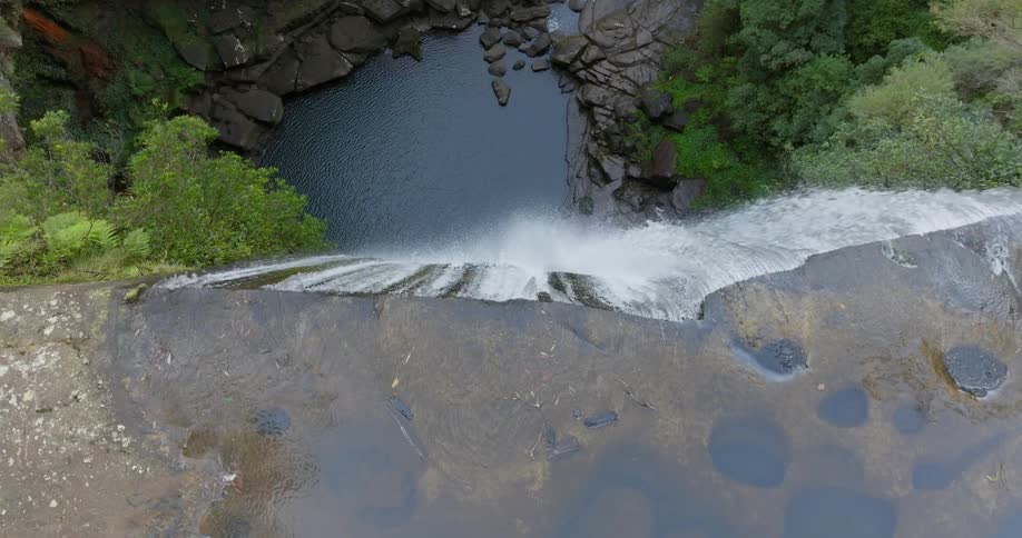 Water flows down waterfall into pool surrounded by bouldersin woods