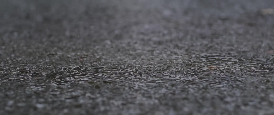Closeup of rain falling on the asphalt generating water droplets and impacts