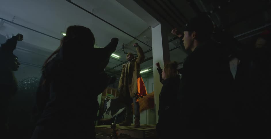 People inside an indoor setting cheering as one of them raises their hand with a clenched fist in the air and others mimic the gesture joining in the excitement