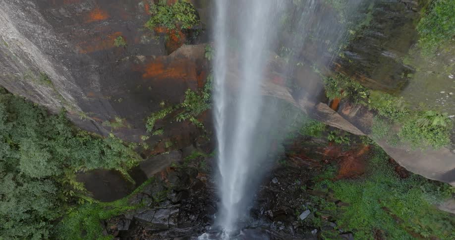 Aerial view of a rainfall next to a mountain flowing into a lake in a valley during day time
