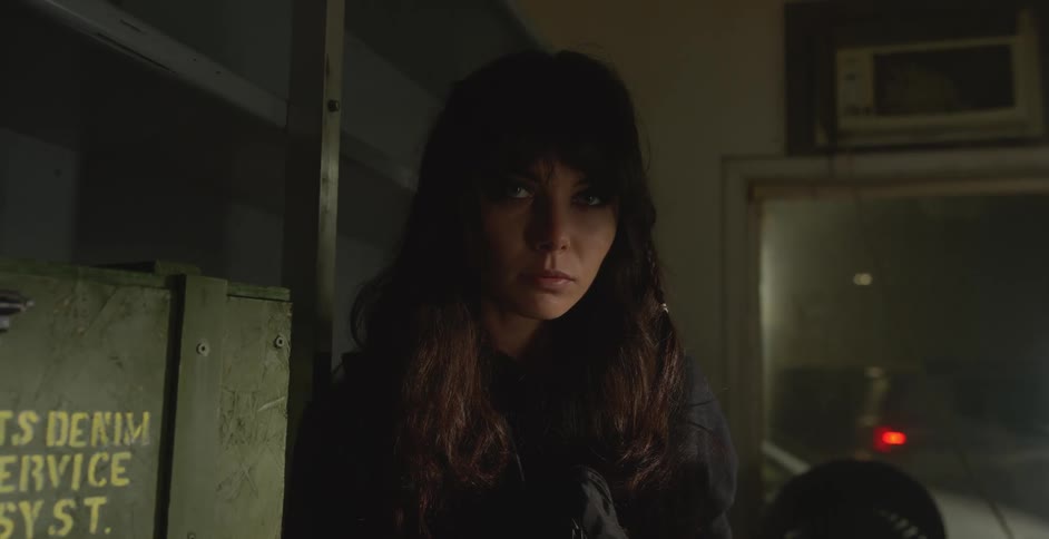 Woman standing next to a metal shelf and a window indoors during night time