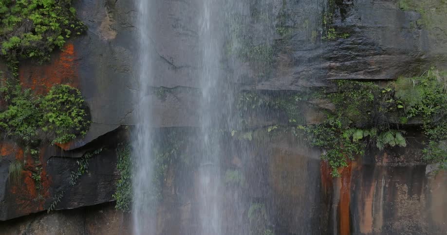 Water cascades down a rocky cliff that is lined with vegetation