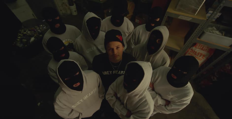 Ten people wearing hoodies and masks stand indoors