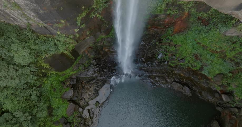 Plants and vegetation grow along the side of a steep cliff as waterfalls flow into the river below